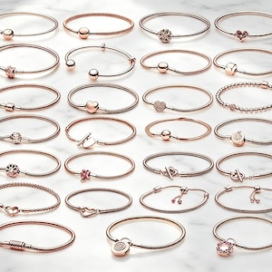 Op de afbeelding: Een collectie van vierentwintig armbanden van roségoudkleurig metaal, gerangschikt in een raster. De armbanden hebben diverse ontwerpen, waaronder slangenkettingen, kralenstrengen en bangles, met verschillende sluitingen, bedels en knevelsluitingen.