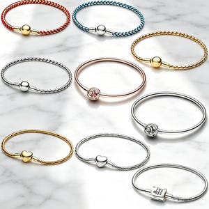 Può includere: Una collezione di nove bracciali con vari design, inclusi cinturini in metallo intrecciato e liscio in tonalità oro, argento, oro rosa, rosso e blu, con chiusure a forma di sfere, rose, cuori e un ciondolo quadrato con testo inciso.