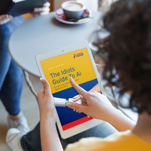 May include: A white tablet displaying a digital publication titled The Idiots Guide To Ai with a yellow, blue, and red graphic design featuring a robotic hand. The screen shows the text Volume 1 August 2024 and Everything you actually know Nothing you don't.