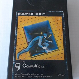 Może przedstawiać: Czarna kaseta z grą wideo Atari zatytułowana Room of Doom firmy CommaVid Inc. Etykieta przedstawia postać ubraną na niebiesko, kucającą na żółtym, teksturowanym tle. Tekst zawiera napisy Room of Doom, CommaVid Inc oraz Video Game Cartridge for use with ATARI Video Computer System, CM-004.