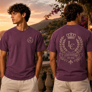 May include: A purple short-sleeved t-shirt featuring a small logo on the left chest and a large graphic on the back. The back design includes a crown, the letters LC, a laurel wreath, and a banner with the text LUXE CULTURE EST. 2026.