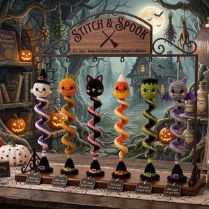 May include: A display stand labelled STITCH & SPOOK featuring six hanging hand-crocheted ornaments: a ghost, a pumpkin, a black cat, candy corn, a green monster, and a purple bat, each with a spiral body and a small black witch hat base.
