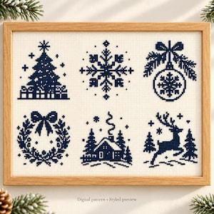 May include: A framed cross-stitch pattern featuring six dark blue holiday icons on a cream-colored fabric background. The designs include a Christmas tree, a snowflake, a bauble, a wreath, a cabin in the woods, and a reindeer, all in a pixelated style.