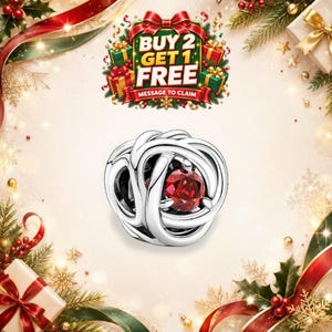 May include: A silver charm bead featuring an intricate, swirling knot design with a single, round, faceted red gemstone set in the center. Above the charm, a festive graphic displays the text BUY 2 GET 1 FREE MESSAGE TO CLAIM.