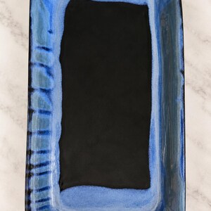 May include: A rectangular ceramic serving tray featuring a deep black center basin surrounded by a vibrant blue glazed border. The rim displays a reactive glaze effect with darker blue and black vertical brushstroke patterns along the edges.