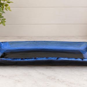 May include: A rectangular ceramic serving tray featuring a glossy finish with a deep black center that transitions into a vibrant cobalt blue rim. The tray has slightly raised edges and a smooth, reflective surface, showcasing a handcrafted aesthetic.