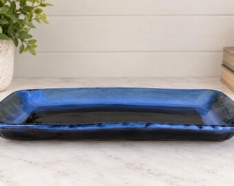 May include: A rectangular ceramic serving tray featuring a glossy finish with a deep black centre that transitions into a vibrant cobalt blue rim. The tray has slightly raised edges and a smooth, reflective surface, showcasing a handcrafted aesthetic.