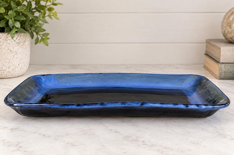 May include: A rectangular ceramic serving tray featuring a glossy finish with a deep black center that transitions into a vibrant cobalt blue rim. The tray has slightly raised edges and a smooth, reflective surface, showcasing a handcrafted aesthetic.