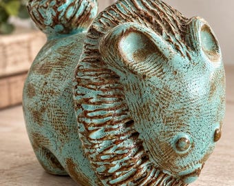 May include: A ceramic lion figurine featuring a textured surface with a turquoise glaze and brown accents. The lion has a prominent mane, rounded ears, and a curled tail, with a distinct cross-hatched pattern visible across its entire body.