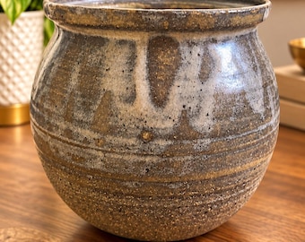 May include: A round ceramic planter with a wide, flared rim. The exterior features a textured, speckled brown and tan base with horizontal grooves and a decorative white glaze drip pattern cascading from the top edge down the sides.