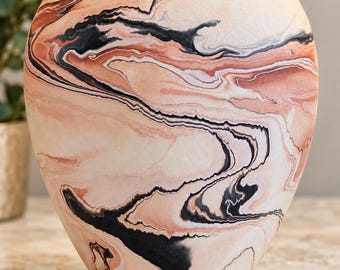 May include: A rounded vase featuring a marbled pattern with swirling colours of cream, soft peach, and deep black. The surface has a matte texture, and the vessel has a wide, curved body that tapers towards a narrow, circular opening at the top.