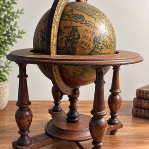 Puede incluir: Un globo terráqueo de estilo antiguo con un mapa en tonos sepia envejecidos y el texto visible Mar Del Zur. El globo está montado sobre un soporte de madera marrón oscuro con un anillo de horizonte circular y cuatro patas decorativas torneadas.