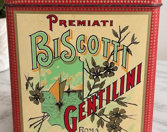 May include: A square red metal tin featuring a cream-colored label with the text Premiati Biscotti Gentilini Roma. The design includes a green illustration of a sailboat on water, dark floral branches, and a border pattern of small gold stars.