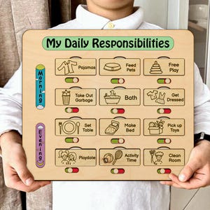 Puede incluir: Un tablero de tareas de madera cuadrado titulado My Daily Responsibilities con filas para tareas de mañana y tarde. Cuenta con doce secciones rectangulares con iconos y etiquetas de texto como Pajamas, Feed Pets, Bath y Clean Room, cada una equipada con un interruptor deslizante para marcar la finalización.