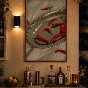 Op de afbeelding: Een rechthoekige ingelijste wandprint met een zilveren ovale schaal met verschillende felrode chilipepers, weergegeven boven een bar met een kom citrusvruchten, een gouden cocktailshaker en drie glazen flessen sterke drank.