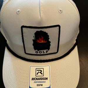May include: A white baseball cap featuring a black rope detail across the base of the crown. A square patch on the front displays a graphic of a dumpster fire with the text GOLF below it. A Richardson Performance sticker is on the brim.
