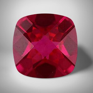 Peut inclure: Une pierre précieuse taille coussin d'une couleur rouge profond et vibrante. La pierre présente une surface à facettes créant un motif géométrique de reflets rouges clairs et foncés sur sa forme carrée aux coins arrondis et finition polie.