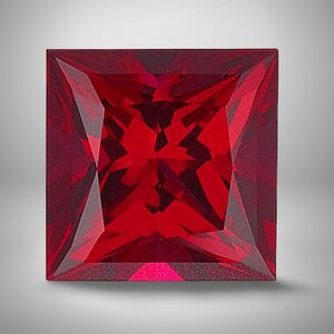 May include: A square-cut gemstone with a deep, vibrant red color. The stone features a faceted surface that creates complex geometric patterns and light reflections across its face, showcasing a sharp, symmetrical four-sided shape.