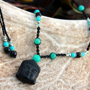 May include: Black Buddha head pendant necklace with turquoise and black beads. The necklace is strung on a black cord and has a matching adjustable cord. The necklace is a unique piece of jewelry.