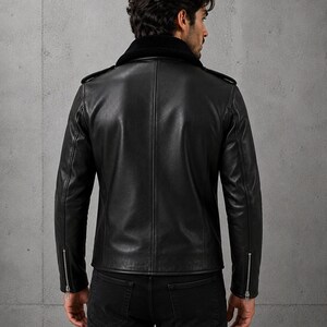 May include: A black leather jacket featuring a dark shearling collar, shoulder epaulets, and silver-toned metal zippers at the sleeve cuffs. The jacket has a smooth finish and a structured back panel design, worn over dark pants.