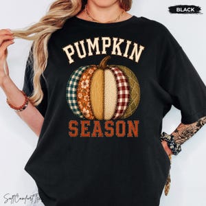 May include: A black t-shirt featuring a graphic of a pumpkin made of various patterned fabric segments, including plaid, floral, and herringbone. The text PUMPKIN SEASON is printed in a bold, orange-toned font above and below the pumpkin graphic.