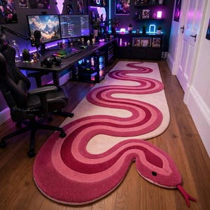 Könnte beinhalten: Ein langer, schlangenförmiger Teppich mit einem Farbverlauf in Rosa- und Magentatönen. Der Teppich hat ein geschwungenes, gewundenes Design mit einem ausgeprägten Kopfbereich, einem kleinen schwarzen Auge und einer herausragenden roten Zungenspitze.