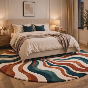 May include: A large circular area rug featuring a repeating wavy pattern in shades of cream, deep teal, and burnt orange. The rug is positioned on a light wood floor beneath a bed with a cream-colored upholstered headboard and matching bedding.