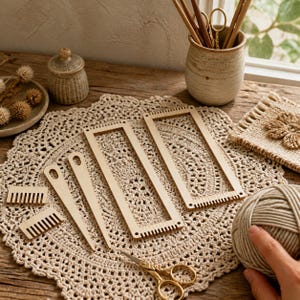 Può includere: Un set di strumenti per tessitura in legno chiaro che include due telai rettangolari con estremità dentellate, due piccoli pettini per tessitura e due lunghi aghi appuntiti, disposti su un centrino all'uncinetto color beige.