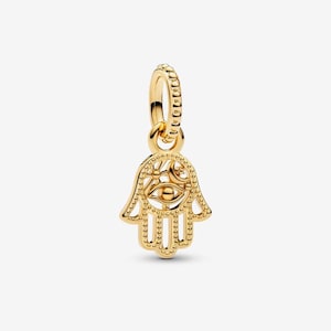 May include: A gold-toned Hamsa hand charm featuring a beaded border and a central eye motif. The palm area includes cut-out details of a crescent moon and small stars. The charm is suspended from a circular, beaded bail for attachment to jewelry.