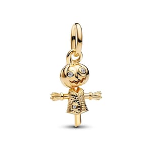 May include: A gold-toned metal charm shaped like a scarecrow with a pumpkin head. The head features two clear, round stones as eyes and a carved mouth. The body wears a textured jacket with a single clear stone detail and outstretched arms.