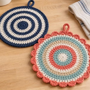 May include: Two round crochet pot holders with hanging loops. One features concentric circles in navy blue and cream. The other displays a scalloped edge with concentric rings in coral, cream, and light blue, showcasing a textured yarn construction.