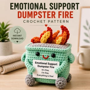 Puede incluir: Un juguete de contenedor de basura tejido a ganchillo en verde menta con ojos negros y una sonrisa roja, rematado con llamas tejidas en amarillo y rojo. Sostiene un letrero blanco que dice: Emotional Support Dumpster Fire, It's fine. I'm fine. Everything is fine!