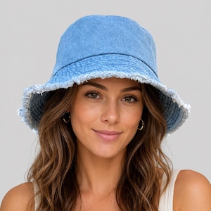 May include: A light blue denim bucket hat featuring a rounded crown and a wide, downward-sloping brim. The edges of the brim are finished with a frayed, distressed fringe detail, providing a textured appearance to the classic cotton fabric.