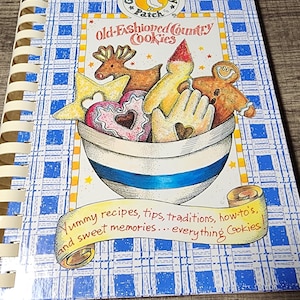 May include: A spiral-bound cookbook titled Old-Fashioned Country Cookies by Gooseberry Patch. The cover features a blue and white plaid pattern, a bowl filled with various shaped cookies, and the text Yummy recipes, tips, traditions, how-to's, and sweet memories... everything Cookies.