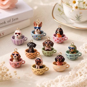 May include: A collection of ten miniature dog charms, each featuring a different breed sitting inside a small, patterned ceramic-style teacup. Each dog wears colorful heart-shaped or round sunglasses, and each charm includes a small gold-tone metal loop.