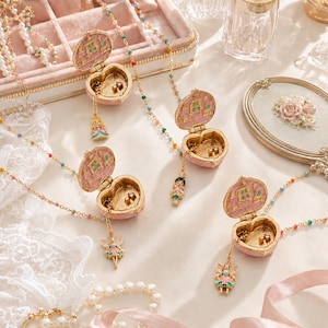 May include: Four heart-shaped locket necklaces with gold-tone chains featuring colourful beads. Each locket opens to reveal a pink interior with a small character charm dangling from the bottom. The lockets are light pink with gold-tone trim.