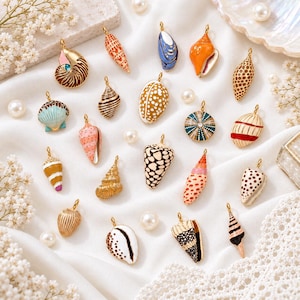 Peut inclure: Une collection de vingt breloques en métal en forme de coquillages, ornées de motifs émaillés variés tels que des pois, des rayures et des couleurs unies. Chaque breloque possède une petite boucle dorée sur le dessus pour la fixation.