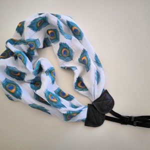 May include: A white camera strap with a peacock feather pattern and black adjustable straps.