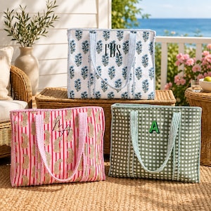 Pode incluir: Três sacos tote retangulares acolchoados com duas alças cada. O saco superior apresenta um estampado floral azul sobre branco com o monograma FBS. O saco inferior esquerdo tem riscas cor-de-rosa e estampado de leopardo com o monograma MA. O inferior direito é de xadrez verde com a letra A.