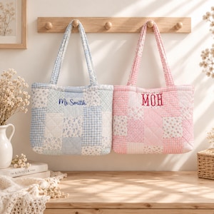 May include: Two quilted tote bags with patchwork designs. The left bag is blue and white with a floral and gingham pattern, featuring the embroidered text Ms. Smith. The right bag is pink and white with a floral and gingham pattern, featuring the embroidered text MOH. Both bags have two shoulder straps.