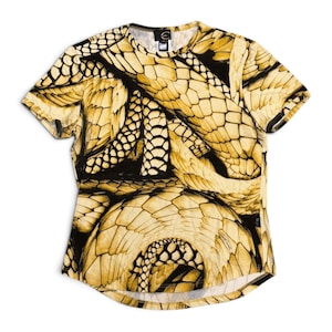 May include: A short-sleeved t-shirt featuring a repeating gold and black snake scale pattern throughout the fabric. The garment has a crew neckline and a curved hemline. A small black brand label is visible at the inner neck area.