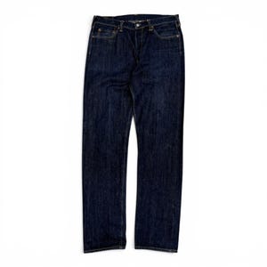 Puede incluir: Un par de pantalones vaqueros de mezclilla azul índigo oscuro con un diseño clásico de cinco bolsillos, cierre de botones, cintura con trabillas para cinturón y remaches de tono cobre visibles en las esquinas de los bolsillos delanteros.