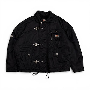 May include: A black jacket featuring a fold-down collar, long sleeves, and a front closure with three silver-toned metal buckles. The garment includes two lower pockets with snap buttons, a zippered chest pocket with an orange logo, and a drawstring hem.