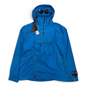 May include: A bright blue hooded jacket featuring a half-zip closure, a large front pocket with two snap-button flaps, and two circular black lenses integrated into the hood and the left sleeve cuff. A black brand tag hangs from the zipper.