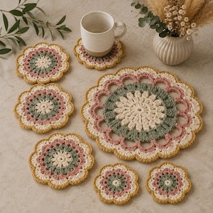 May include: A set of round, crocheted doilies and coasters featuring a floral-inspired pattern in cream, sage green, dusty rose, and mustard yellow. The set includes one large circular mat and six smaller coasters, all with scalloped edges.