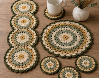 May include: A set of crocheted table linens featuring a circular floral pattern in shades of sage green, mustard yellow, and cream. The collection includes a long runner, one large placemat, and four small coasters, all with scalloped edges.