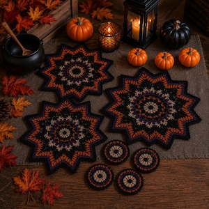 May include: Two large star-shaped crochet mats and four small circular crochet coasters featuring a black, orange, and purple geometric pattern. The mats and coasters are arranged on a brown fabric surface alongside several small pumpkins and a lantern.