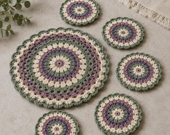 May include: A set of one large and five small circular crochet doilies featuring a concentric pattern in shades of sage green, cream, and muted purple. Each piece has a scalloped edge and a textured, floral-inspired design made of yarn.