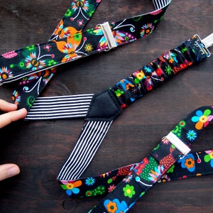 Può includere: Bretelle nere con un motivo floreale colorato. Le bretelle hanno cinturini regolabili e clip metalliche.