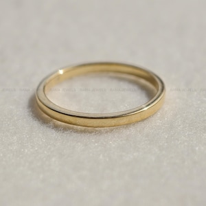 May include: A simple, polished gold band ring with a smooth, rounded surface. The ring features a consistent, uniform width throughout its circular design, showcasing a bright, reflective metallic finish that catches the light evenly across its surface.